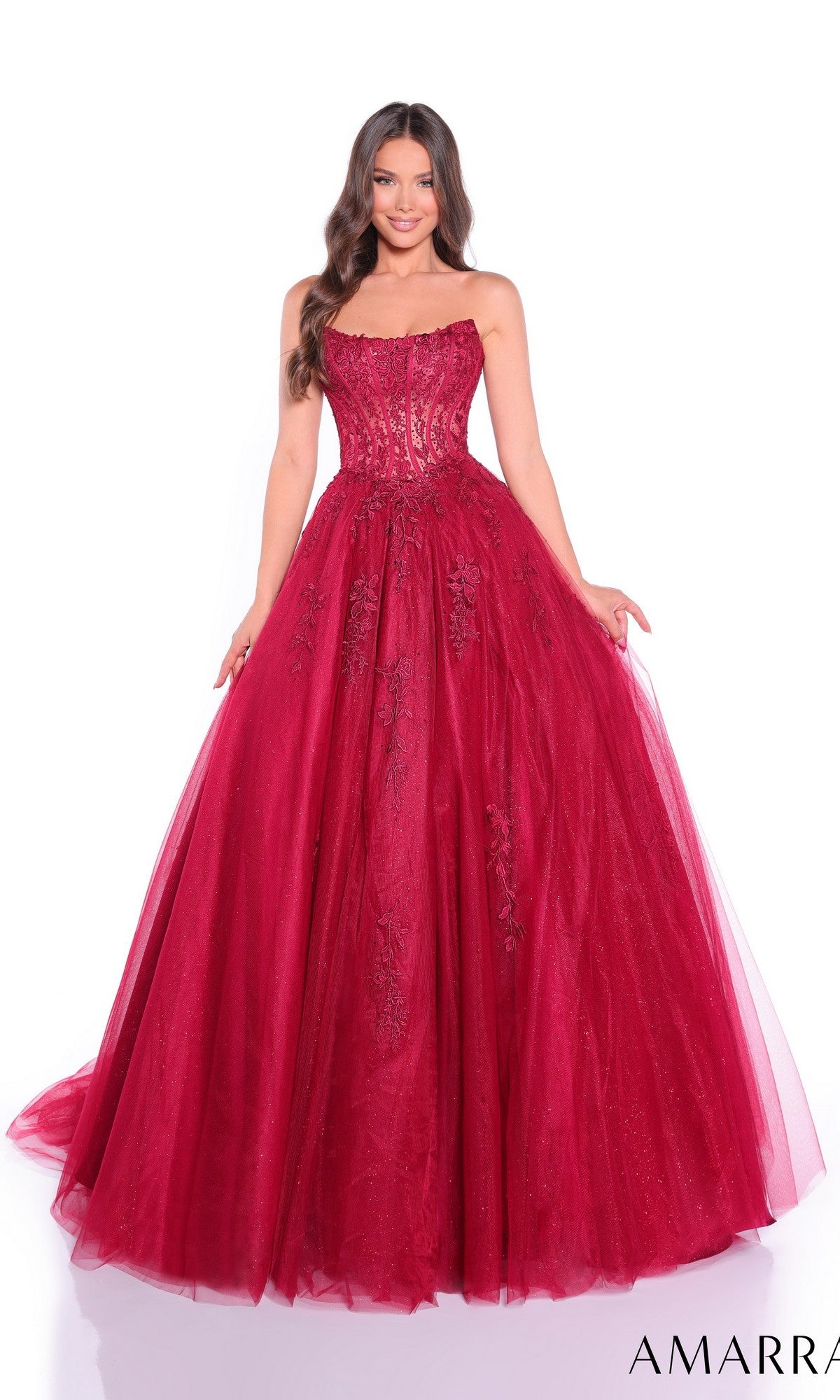 A woman poses against a white background wearing the Amarra 88913, a strapless long prom ball gown featuring a sheer lace corset and floral lace details.